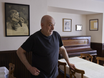 Iñaki Urdiroz, propietario del Hostal Burguete, en el comedor junto al piano y el cuadro de Hemingway.	 JESÚS GARZARON