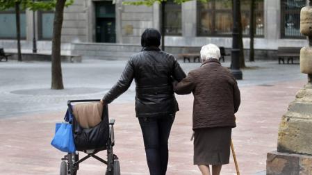 Una persona pasea con una anciana dependiente.