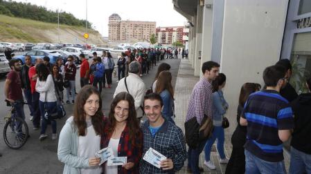Tres aficionados rojillos posan orgullosos con sus entradas mientras cientos de personas hacen cola a sus espaldas para adquirir una.