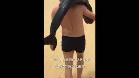 Graban a un hombre con un delfín al hombro paseando por una playa china