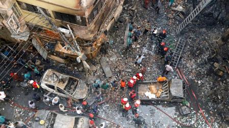 Varios bomberos inspeccionan los escombros tras el incendio declarado en la madrugada de este jueves en el barrio Chawkbazar del casco viejo de Dacca (Bangladesh).