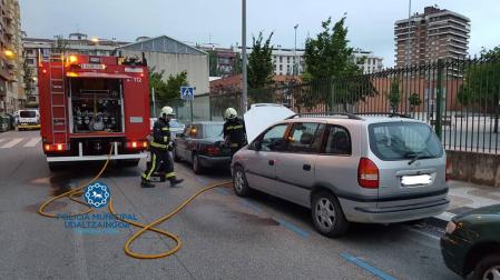 Los bomberos sofocan el fuego generado en un coche al arrancarlo, en la calle Pintor Maeztu.