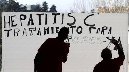 Dos personas teminan de pintar un cartel sobre un cristal en el Complejo Hospitalario de Navarra en favor del tratamiento de la Hepatitis C.