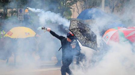 Un protestante antigubernamental arroja un bote de gas a los policía.