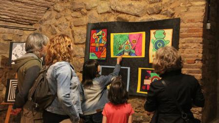 Padres y alumnos contemplan una exposición de pintura abstracta realizada por escolares.