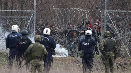 Un grupo de migrantes intenta de cruzar la frontera griega, mientras la policía trata de evitarlo lanzando botes de gases lacrimógenos