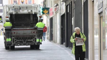 Una mujer regresa de comprar el pan y la prensa en Pamplona. Al fondo, el servicio de recogida de basuras, que sigue funcionando.