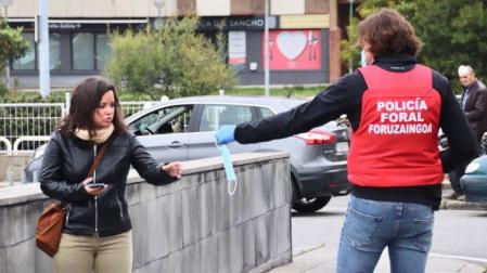 Un policía foral reparte una mascarilla a una mujer.
