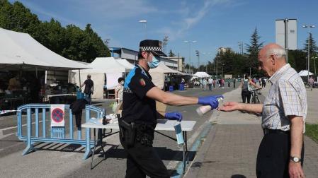 Un agente proporciona gel desinfectante y mascarilla a una persona en el acceso al mercadillo.