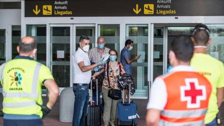 Dos viajeros reciben las indicaciones de los servicios de emergencias tras desembarcar en Lanzarote de un vuelo procedente de Madrid en el que parte del pasaje ha sido sometido a aislamiento después de que uno de los ocupantes del avión diera positivo en covid-19 en unas pruebas cuyos resultados tenía pendiente.