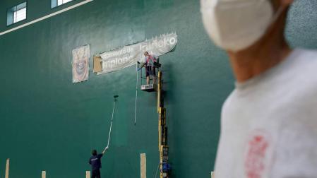 Dos operarios de la Federación Navarra de Pelota pintan la pared izquierda del Labrit este lunes por la mañana.