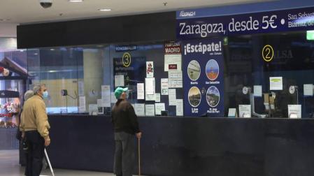 Varias personas aguardan en la taquilla de la estación de autobuses.