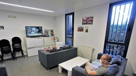 Usuarios del centro para personas sin hogar de Triniarios ven la televisión guardando la distancia.