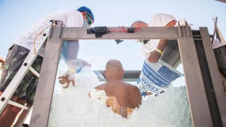 El nadador de hielo austriaco Josef Koeberl en una cabina de vidrio mientras los voluntarios la llenan con cubitos de hielo.