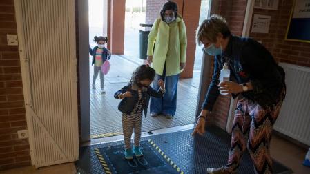 Daniela, de 4 años, desinfecta sus zapatos tras soltar a su madre, con abrigo amarillo, Marta Sampedro.