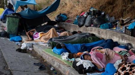 Migrantes del campo de Moria duermen junto a una carretera.