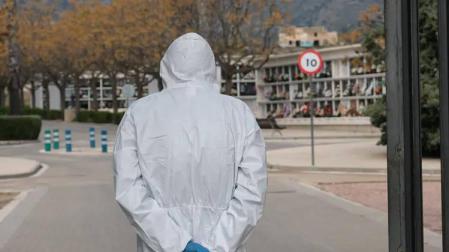 Una persona con un traje de protección, frente un cementerio.
