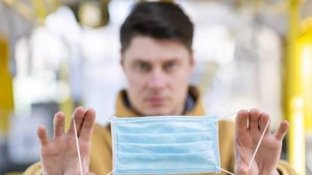 Un hombre sostiene una mascarilla quirúrgica entre sus manos