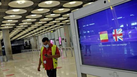 Un operario de Iberia pasa al lado de un monitor con las banderas de España y Reino Unido en la T1 del Aeropuerto de Madrid-Barajas.