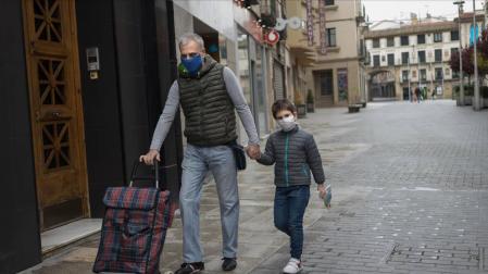 Un niño camina por la calle con su padre, ambos con mascarillas, en Tudela