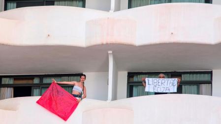 Dos de los jóvenes en aislamiento en el hotel Palma Bellver portan dos pancartas pidiendo salir