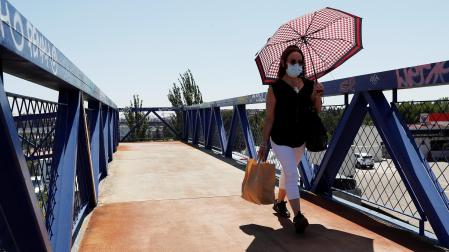 Una mujer con mascarilla se protege del sol cuando cruza por una pasarela en Madrid
