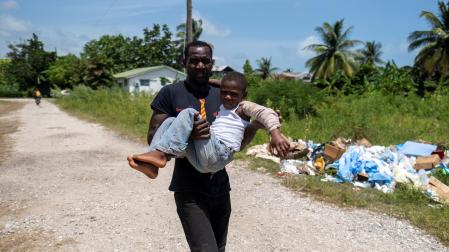Hombre carga a un niño herido hacia un centro medico para que reciba tratamiento en Les Cayes