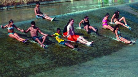 Varios de los participantes en la ludoteca de la Txantrea se deslizan por la presa del río Arga junto a uno de los monitores