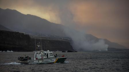 Un barco navega cerca de la columna de humo y la lava del volcán de Cumbre Vieja