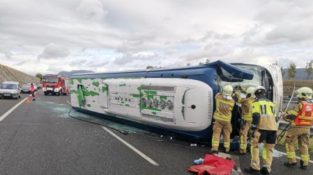 Bomberos atienden a los afectados en el accidente con un autobús volcado.