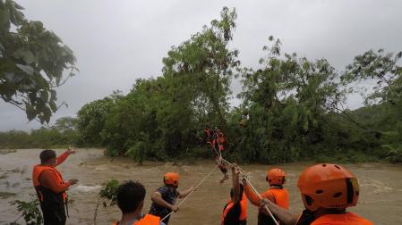 Equipos de rescate ayudan a una persona a pasar sobre un río en la provincia filipina de Gonzaga