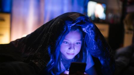 Una niña mira una pantalla por la noche