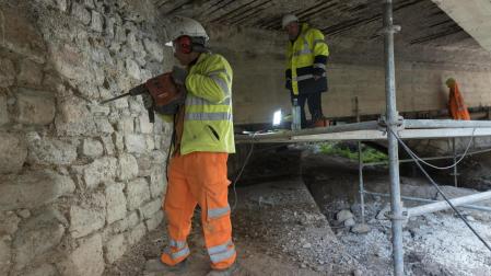 Dos operarios trabajan en los arcos del puente más cercanos al casco urbano de Tudela