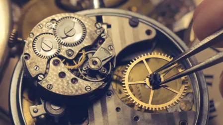 Una mano con pinzas manipula las piezas minúsculas de un reloj antiguo.