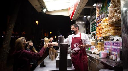 Dos chicas en un tenderete de comida en la Feria de Reyes de la Gran Vía de Barcelona, cubiertas con mascarillas