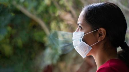 Una mujer protegida con una mascarilla observa a través de una ventana