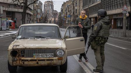 Un miembro de la Guardia Nacional habla con el conductor de un vehículo semidestrozado en el centro de Kiev