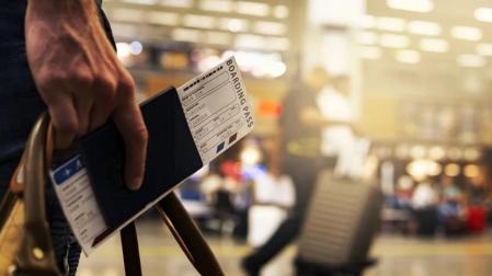 Una persona sostiene su pasaporte y el billete de avión