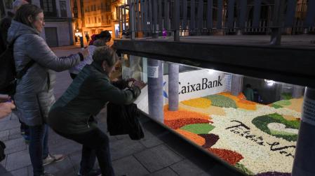 Varias personas fotografían el tapiz de verduras colocada en los bajos del quiosco de la plaza de los Fueros