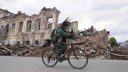 Un ucraniano monta en bicicleta frente a un edificio destruido en Kharkiv, Ucrania