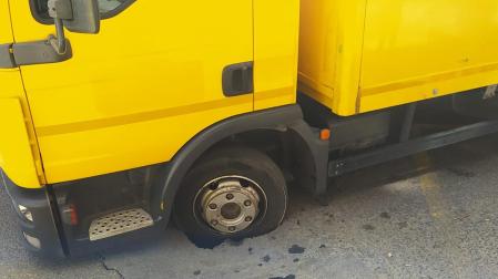 El camión de reparto de Correos con la rueda atrapada en el asfalto