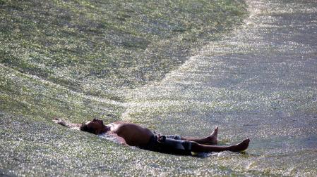 Un hombre se refresca los pasados días de ola calor junto a las pasarelas del río Arga en Pamplona