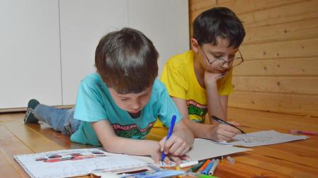 Dos niños, uno de ellos con gafa, dibujan en el suelo