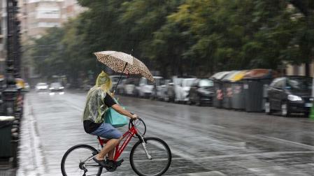 Un hombre circula en bicicleta bajo la lluvia en Valencia