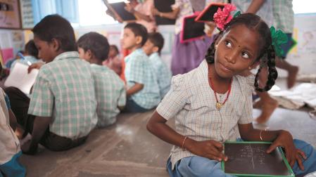 Una niña india escribe unos números en su pizarra, en la escuela