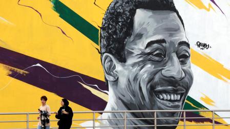 Unas mujeres pasan delante de un mural que representa al exjugador brasileño Edson Arantes do Nascimento, "Pelé" enfrente del estadio Al Khalifa de Doha, Catar