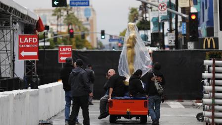 Varios operarios mueven una estatua de un Oscar en el exterior del Dolby Theatre en Hollywood durante los últimos preparativos para la entrega de los premios.