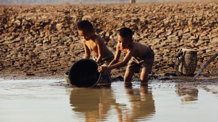 Dos niños juegan con un cubo en la orilla de un río.