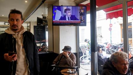 Una televisión en un bar de París muestra la entrevista al presidente francés Emmanuel Macron en la que ha defendido la reforma de las pensiones que aumenta la edad de jubilación de 62 a 64 años