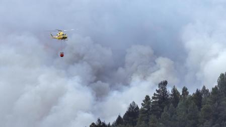 Un helicóptero sobrevuela la columna de humo del incendio forestal declarado este jueves en el término municipal de Villanueva de Viver, en la zona limítrofe de las provincias de Castellón y Teruel